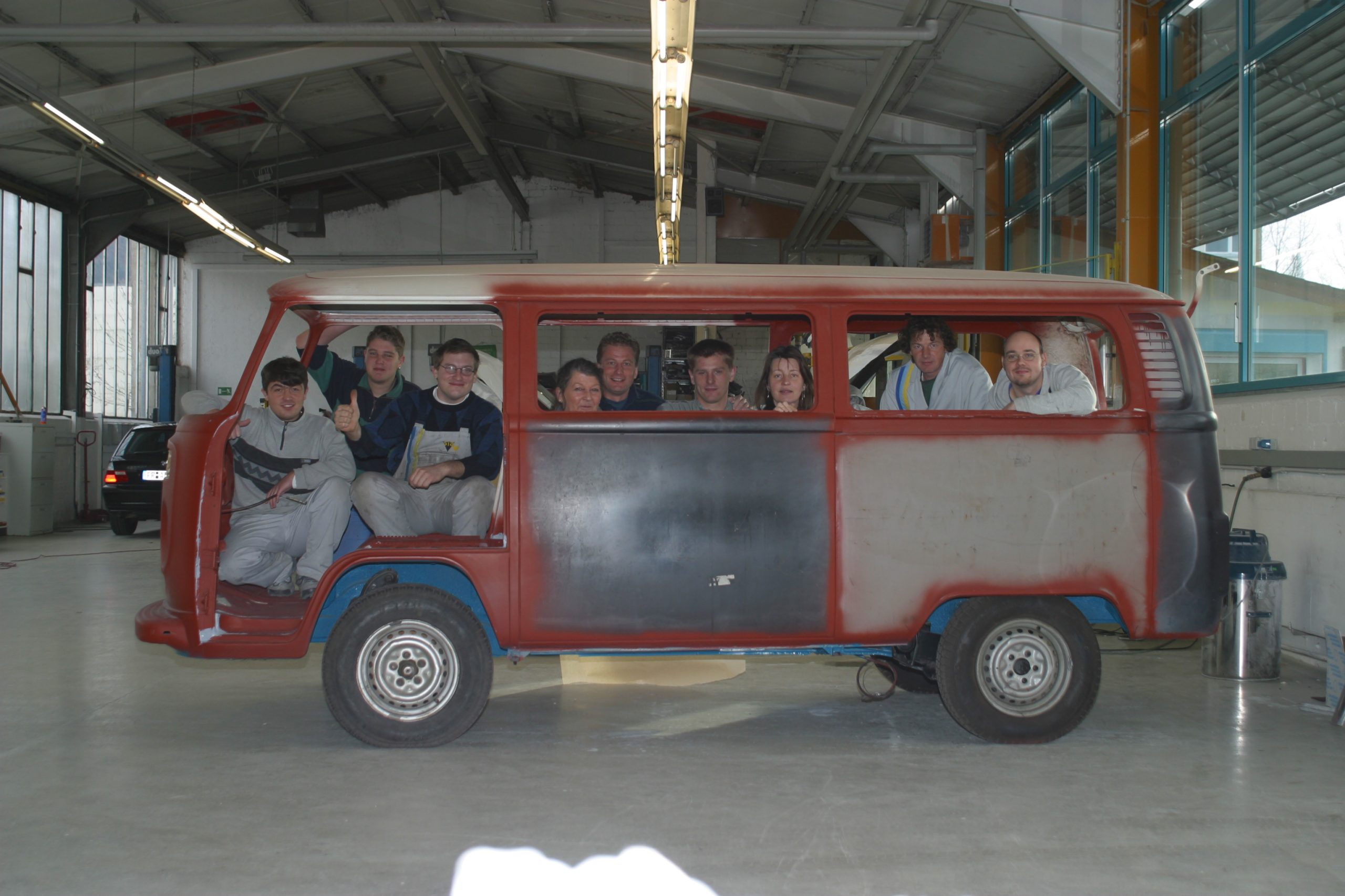 Team von Fred Bank sitzt gemeinsam im teilweise lackierten VW T2 Bus in der Werkstatt